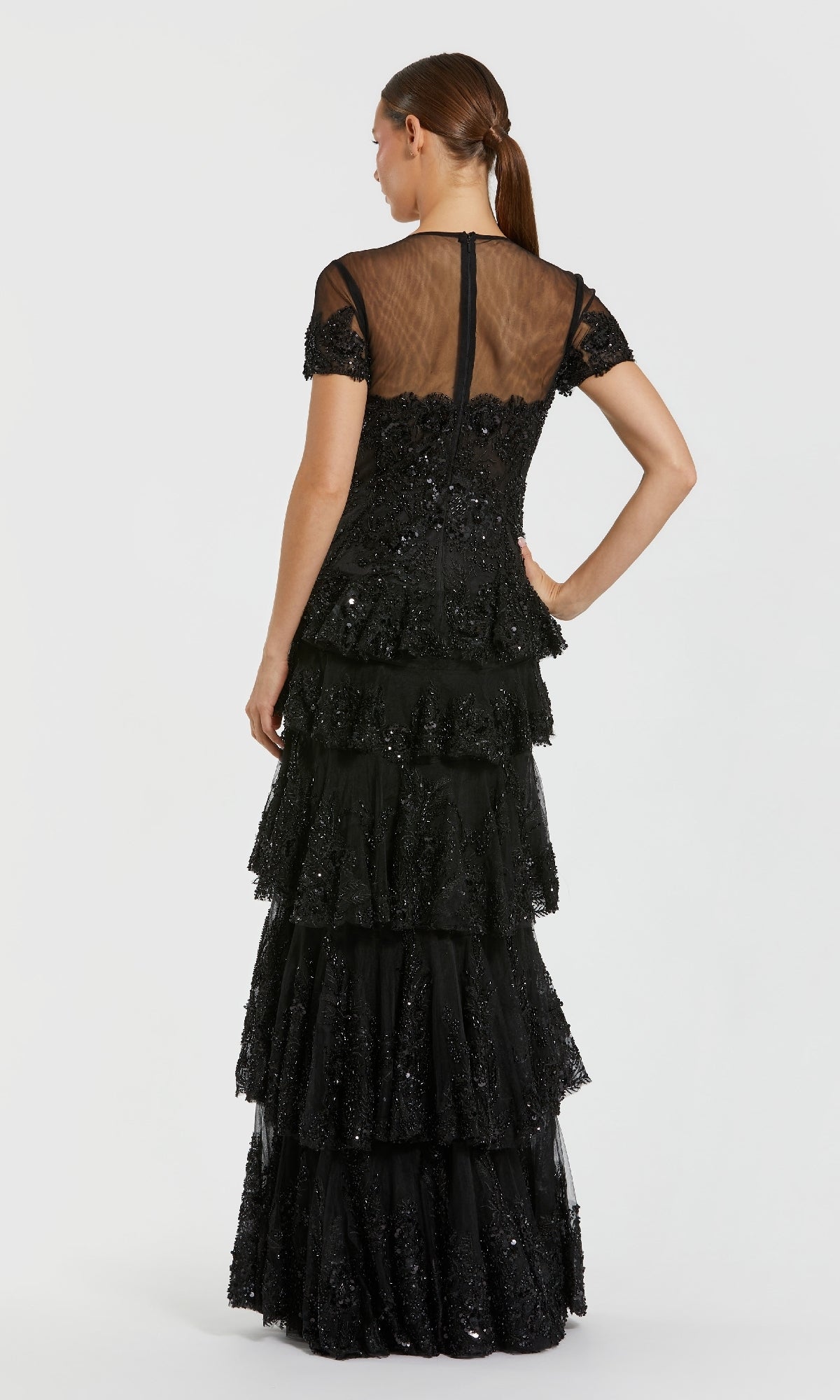 Woman showing the back of a tiered black evening gown standing in front of a white background